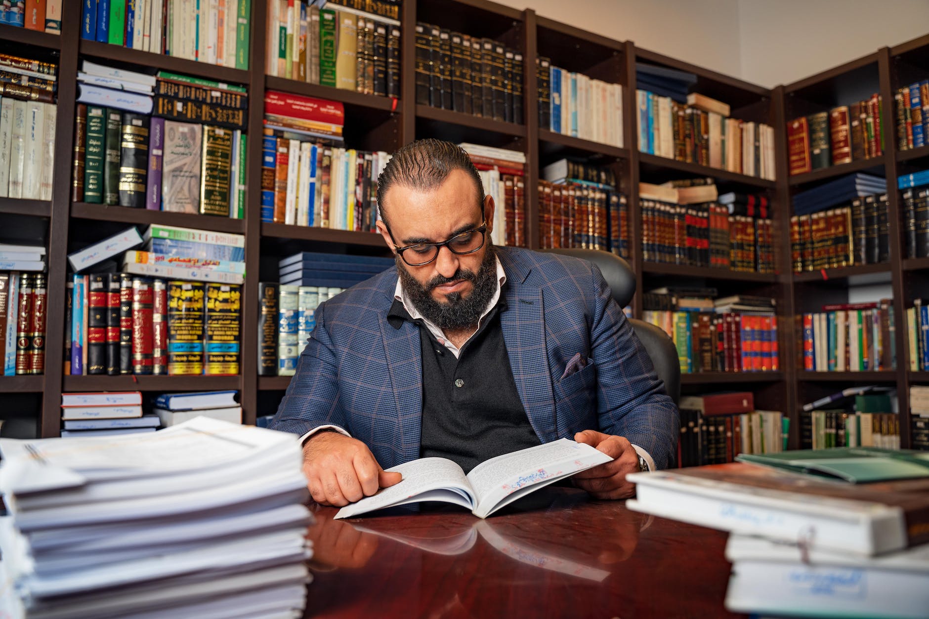bearded man in the library wearing eyeglasses while reading a book
